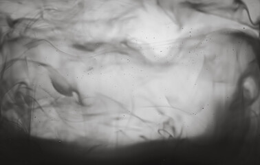 A black and white photo of smoke with a grey background. The smoke is thick and dark, giving the image a moody and mysterious feel