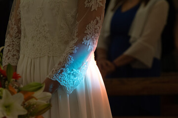 Bride holding bouquet is standing in church with light shining on her dress