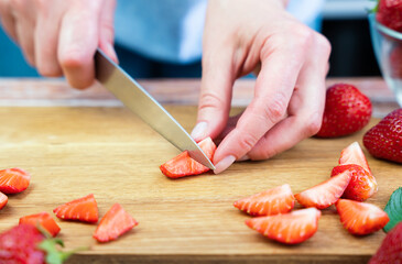 Woman cutting strawberry for lemonade on the table in the kitchen. Close-up. Selective focus.