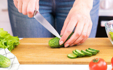 Young woman cuts cucumbers. Cooking vegetable salad. Healthy eating concept. Close-up. Selective focus.