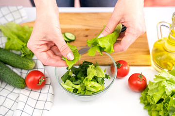 Woman's hands puting lettuce leaves in a glass bowl. Cooking vegetable salad. Close-up. Selective focus.