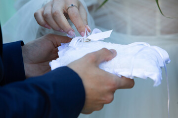 Bride and groom holding a white wedding ring pillow with a satin ribbon
