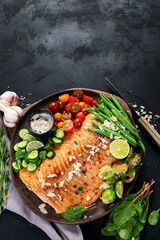 Cooked salmon with fresh vegetables, lime and souce. Baked fish on dark background