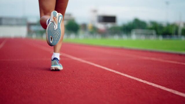A woman is running on a track with her legs apart. She is wearing blue and white shoes