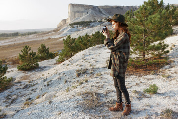 Stylish woman in plaid shirt and hat capturing a moment with her camera on a sunny day