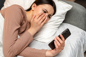 Young girl, teenager getting upset while reading bad news on smartphone in bed