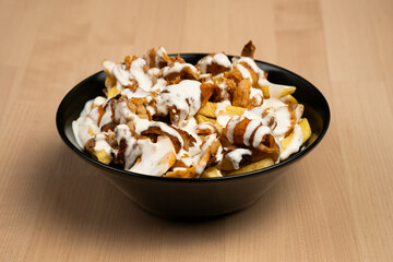 Bowl of loaded fries topped with creamy sauce and grilled chicken on a wooden table