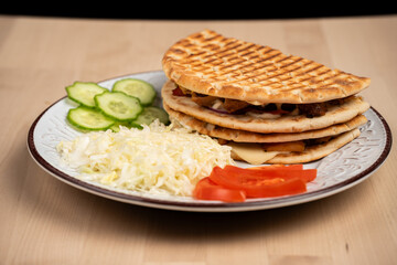 Plate of grilled pita sandwiches with shredded cabbage, cucumber slices, and tomato slices