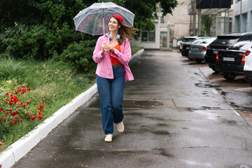 Smiling happy woman and rain feeling water in the city with umbrella, freedom and happiness