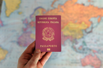 Fototapeta premium Man holding Italy passport in hand and world map in background