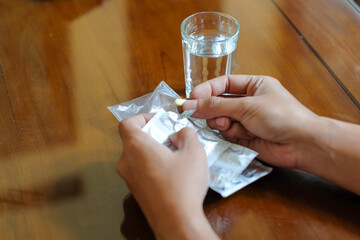Close up of a hands taking a pill from a blister with a water glass on a wood table, for medical and healthcare concept.
