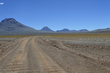 Estrada de terra com vulcões ao fundo