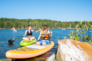 11 year old boy and teenage girl on SUP boards on the lake. brother and sister spend their holidays on a stand-up  paddle board on the river