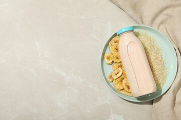 Bottle with milk on plate with rice and sliced bananas, towel on beige background, space for text