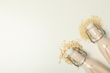 Bottles with milk, oatmeal and sesame seeds on white background, space for text