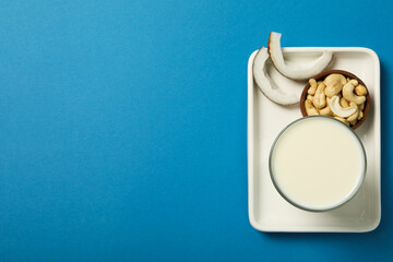Glass of alternative milk, coconut and nuts in bowl on blue background, space for text