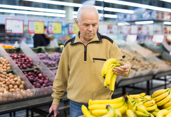 Elderly man choosing banana in supermarket