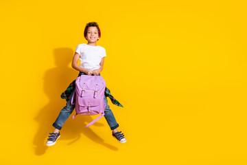 Full body photo of cute little boy hold backpack jumping dressed stylish white clothes isolated on yellow color background