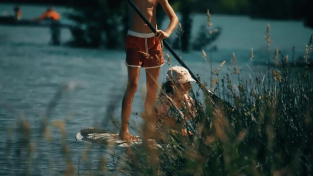 Happy little girl and unknown boy paddle a paddle board or SUP, romantic summer vacation time