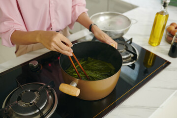 High angle view of young woman boiling greens for korean dish on the stove