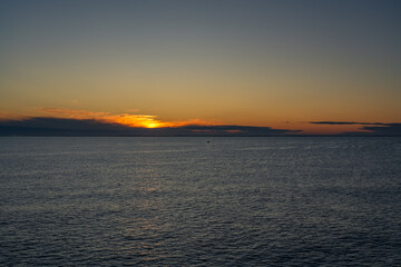 A small solitary fishing boat sails across the calm waters of the Skagerrak Sea, with the rising sun casting a golden glow on the horizon near the coast of Norway