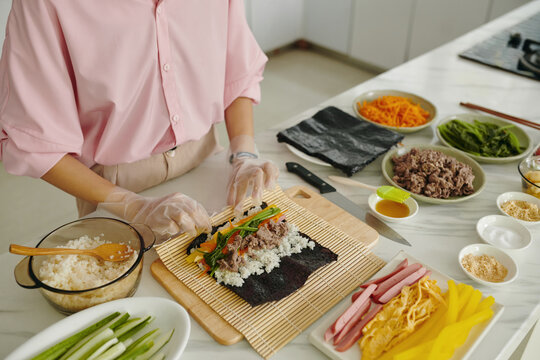 Close-up of woman in gloves making korean kimbap from vegetable and meat in the kitchen