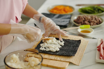 Close-up of woman putting rice on nori while making korean kimbap at home