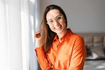 Smiling woman in eyeglasses looking at camera while posing at home