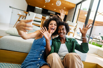 A young couple of African descent is sitting in a modern living room, both smiling and enjoying...