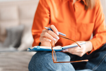 Closeup of unrecognizable woman holding eyeglasses and notebook while studying