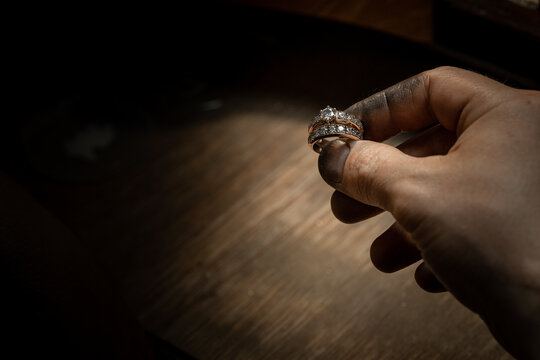 Closeup of a diamond wedding ring and dirty jeweller hands holding it