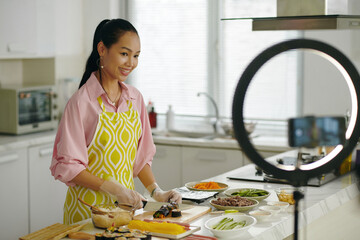 Asian young woman making her food vlog while standing in the kitchen