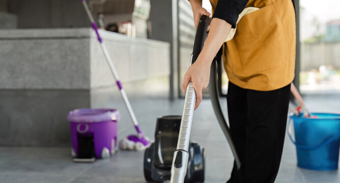 Female Employee Cleaning Coffee Shop with Vacuum Cleaner and Mop in Modern Cafe Setting