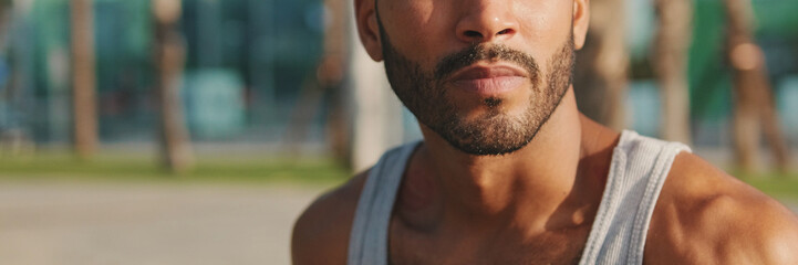 Fototapeta premium Young bearded male athlete is resting after training sitting on bench on modern background, close up, panorama