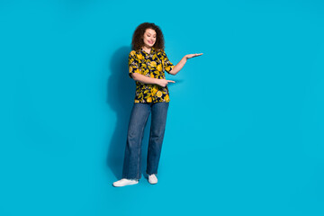 Full length photo of adorable lovely girl wear print shirt measuring arm showing empty space isolated blue color background