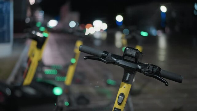 Blurred view of parked electric scooters with distinctive night lights in the background, with soft bokeh effects from the streetlights