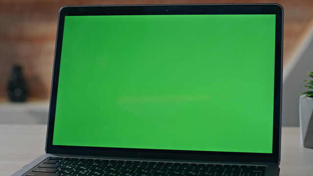 Empty chroma key laptop display on workplace desk closeup. Green screen computer