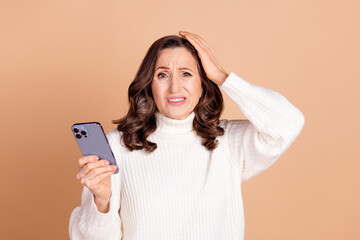Photo of worried nervous senior woman wear white stylish clothes hold iphone isolated on beige...