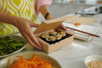 Close-up of woman packing homemade sushi in carton box
