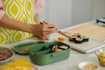 Close-up of housewife packing kimbap with sticks in lunchbox