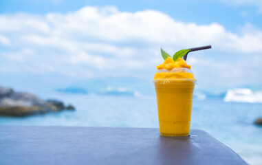 Smoothie made from fresh mango fruits against the backdrop of a seascape. Fruit and yoghurt ice cream decorated with leaves. Glass of tropical dessert close-up.