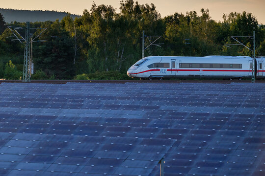 Gro&szlig;er Solarpark. Im Hintergrund verl&auml;uft die auf vier Gleise ausgebaute Bahnstrecke zwischen Bamberg und N&uuml;rnberg, auf der ein ICE-4 aus Berlin in Richtung M&uuml;nchen rollt. 