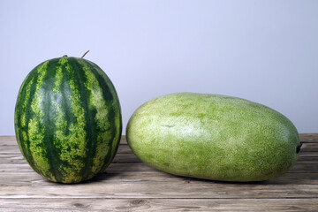 Two watermelons of different varieties lie on a wooden table.