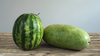 Two watermelons of different varieties lie on a wooden table.