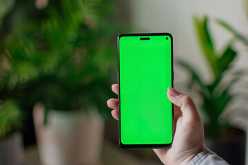 In a close-up shot, a hand holds a smartphone with a vibrant green screen, perfect for displaying app mockups or promotional content - Powered by Adobe