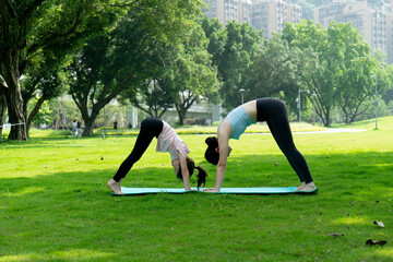 Fototapeta premium Mom and daughter are doing yoga on the park lawn