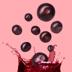 Acai berries falling into juice on pink background