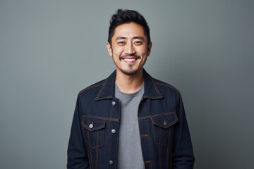 Obraz premium Portrait of a satisfied asian man in his 30s sporting a rugged denim jacket isolated in minimalist or empty room background