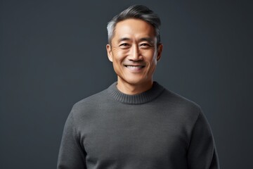 Naklejka premium Portrait of a happy asian man in his 50s wearing a cozy sweater in minimalist or empty room background
