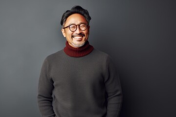 Portrait of a happy asian man in his 50s wearing a cozy sweater on minimalist or empty room background